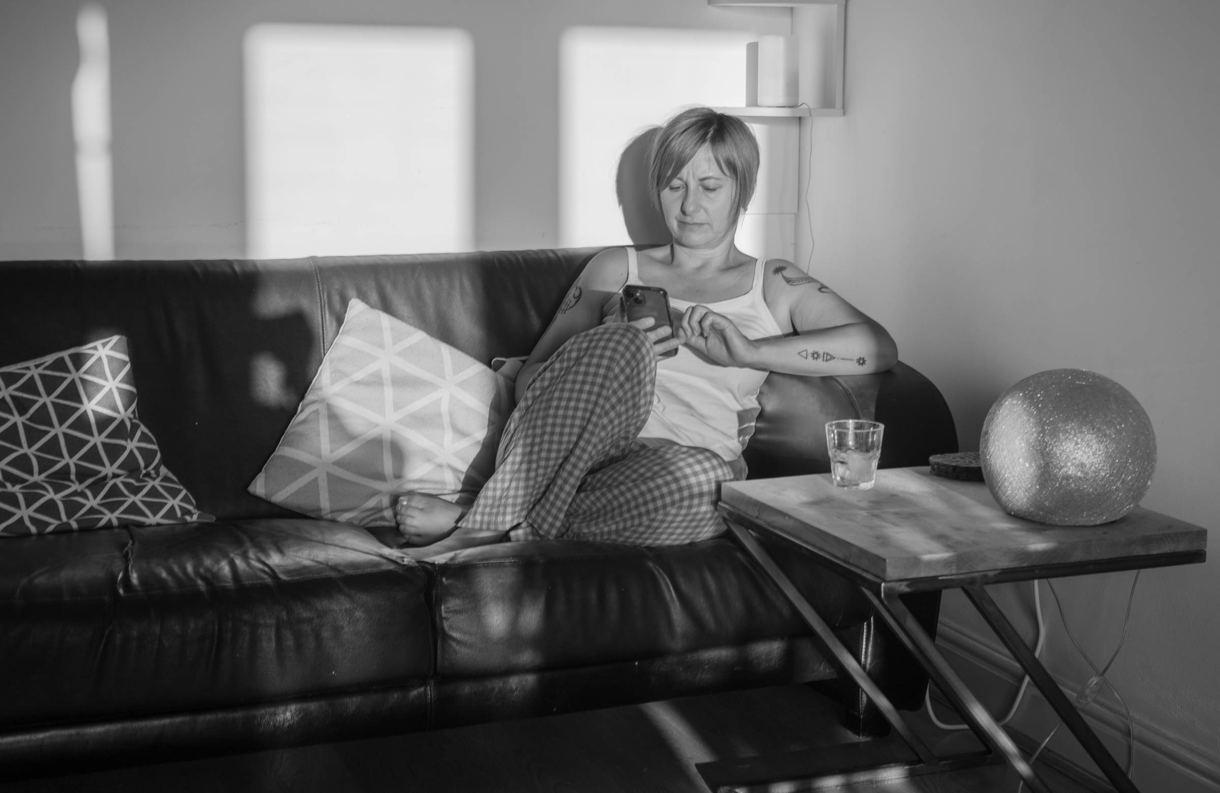 Black and white photo of woman sitting on a sofa and browsing on her mobile phone.