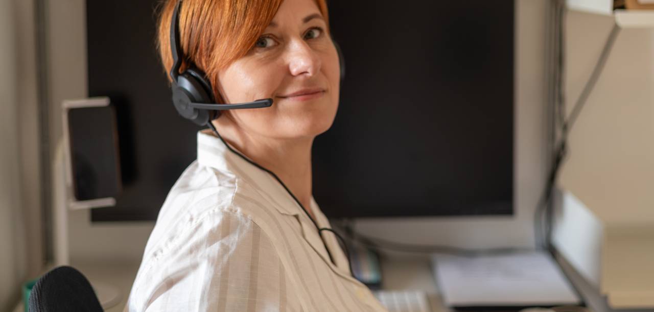 Colour image of a conference interpreter sitting at her home office desk with her headset on.