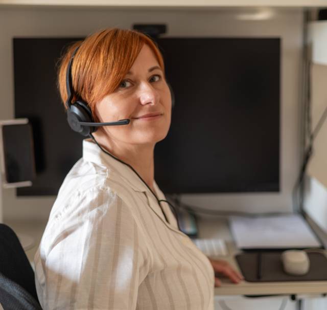 Colour image of a conference interpreter sitting at her home office desk with her headset on.