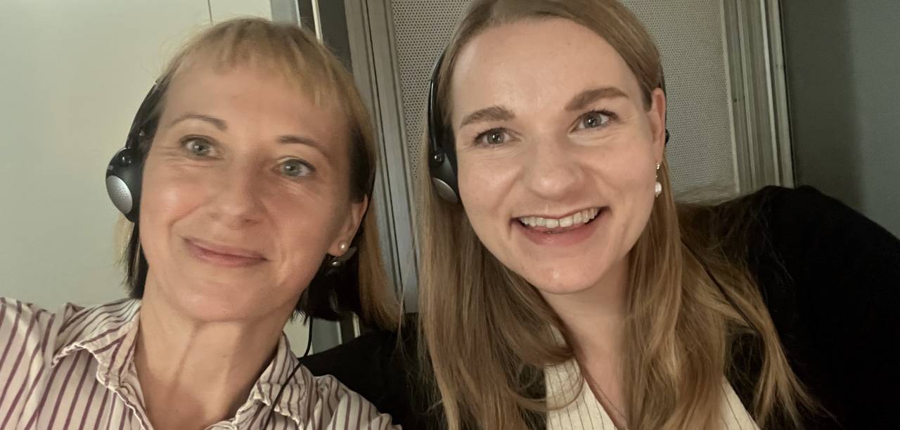 Two interpreters in the booth: the image shows an image of two smiling women wearing headsets.