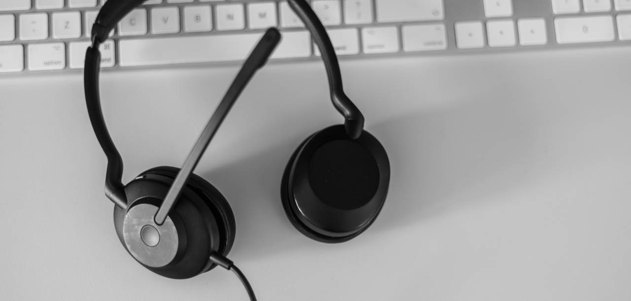 Black and white image of a headset on a white desk and keyboard.