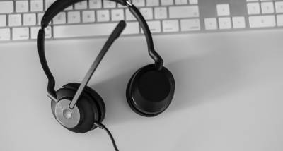 Black and white image of a headset on a white desk and keyboard.