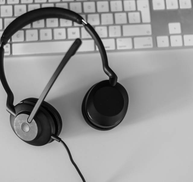 Black and white image of a headset on a white desk and keyboard.