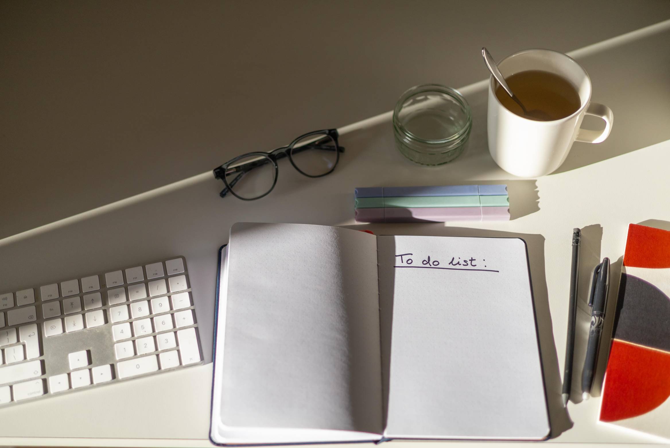 A conference interpreter home office desk featuring a keyboard, a notebook with a to-do-list, glasses and a tea mug.