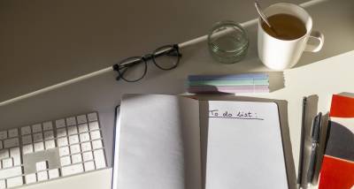 A conference interpreter home office desk featuring a keyboard, a notebook with a to-do-list, glasses and a tea mug.