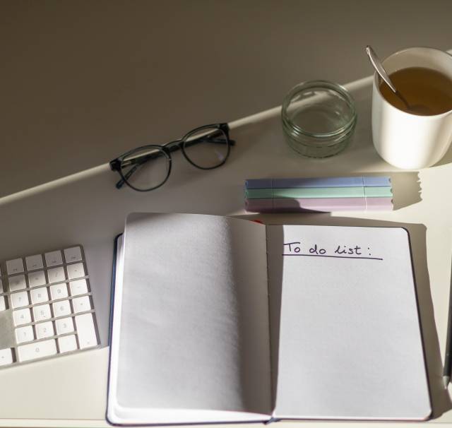 A conference interpreter home office desk featuring a keyboard, a notebook with a to-do-list, glasses and a tea mug.