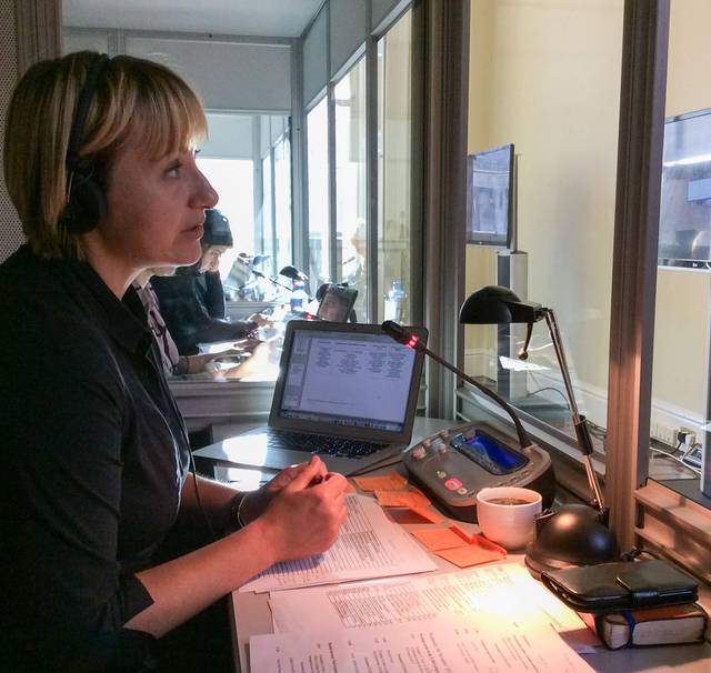 Conference interpreter in the booth wearing a headset and looking at a large screen.